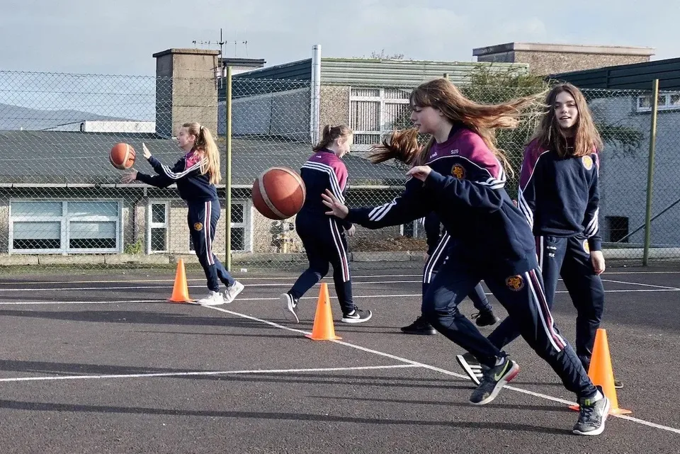 Studentesse del McEgan College giocano a calcio su un campo sportivo all'aperto con edifici sullo sfondo.