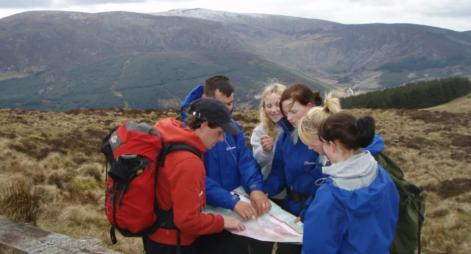 Un gruppo di studentesse e studenti della Balla Secondary School si trova in abbigliamento da montagna in un paesaggio montano sotto un cielo nuvoloso.