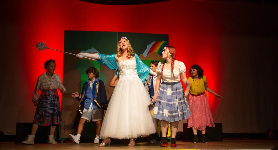 Studenti della Ojai Valley School recitano in uno spettacolo teatrale in costume su un palcoscenico illuminato.