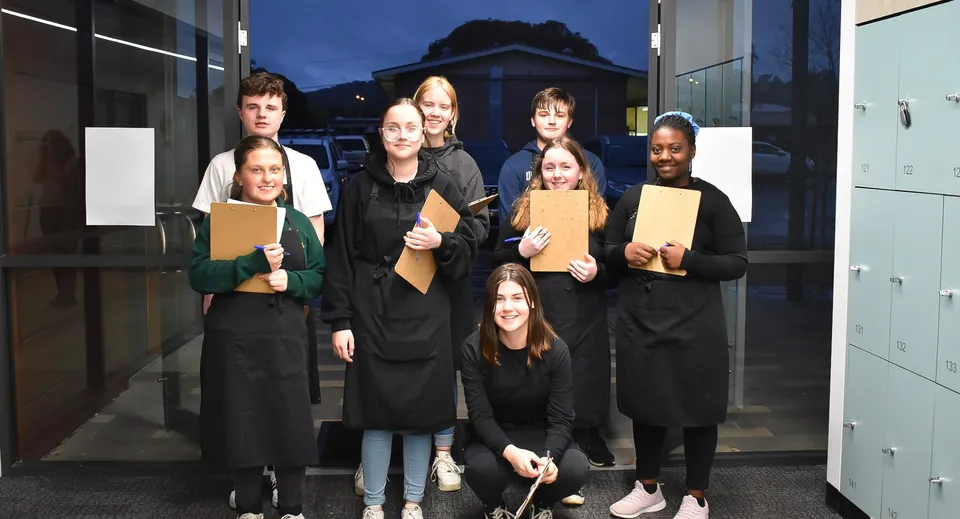 Un gruppo di studenti si trova di notte con dei faldoni davanti a un edificio all'interno del campus della Grant High School.