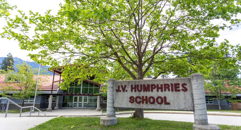 Un grande albero dal folto fogliame verde si trova all'ingresso dell'edificio scolastico della J.V. Humphries Secondary School.