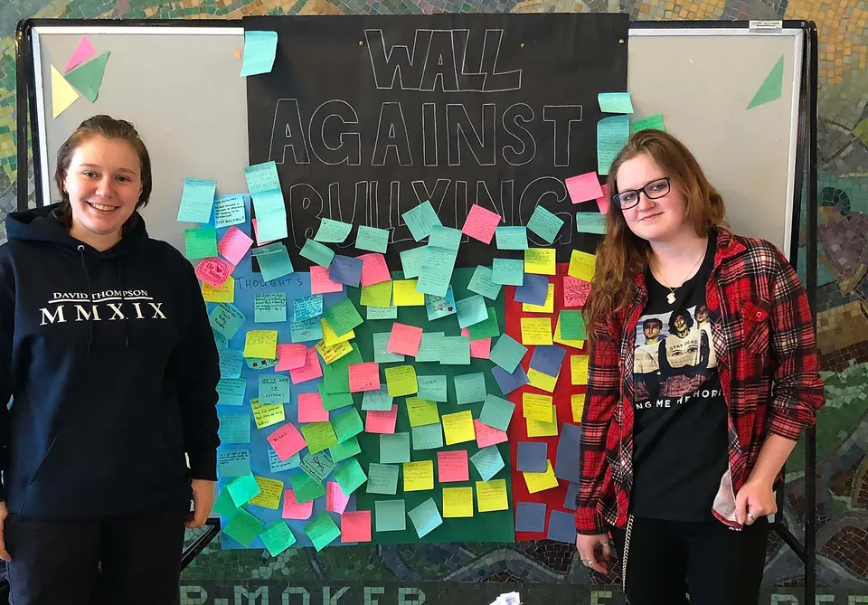 Due studentesse davanti alla parete anti-bullismo con foglietti colorati presso la David Thompson Secondary School.