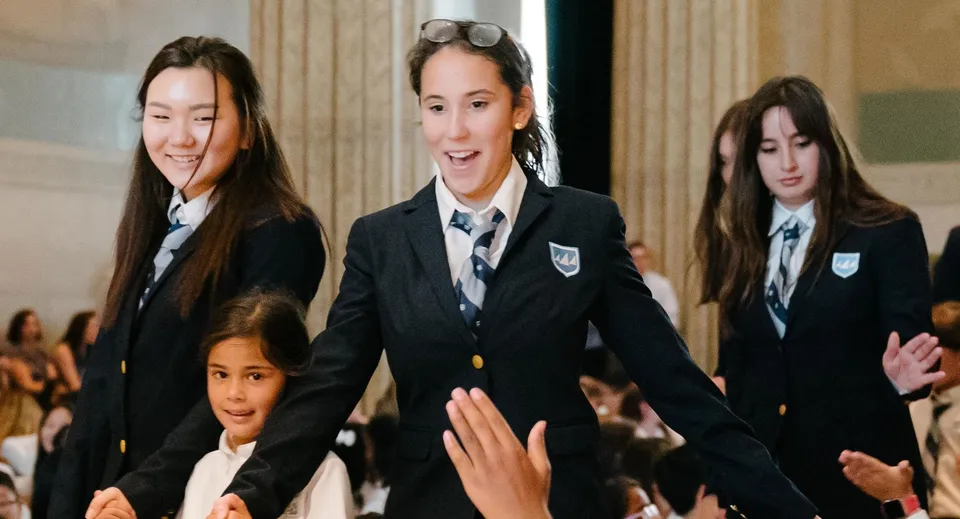 Un gruppo di studenti in uniforme scolastica è insieme davanti alla Léman Manhattan Preparatory School in un contesto formale.