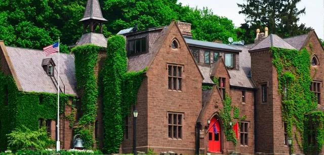 Das Backsteingebäude der Hoosac School mit roter Tür ist von grüner Vegetation umgeben und zeigt im Vordergrund eine amerikanische Flagge.