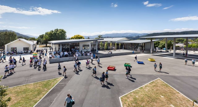 All'esterno dell'Upper Hutt College si vede una piazza del mercato animata con diversi banchi e montagne sullo sfondo.