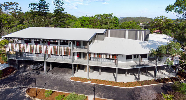 Das moderne mehrstöckige Gebäude der Cavendish Road State High School steht umgeben von bewaldeter Landschaft.