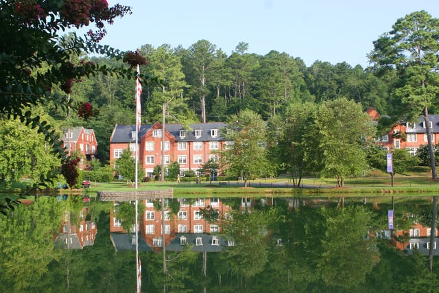 Un laghetto all'interno del campus della Darlington School riflette gli edifici in mattoni rossi e il paesaggio boschivo verde circostante.
