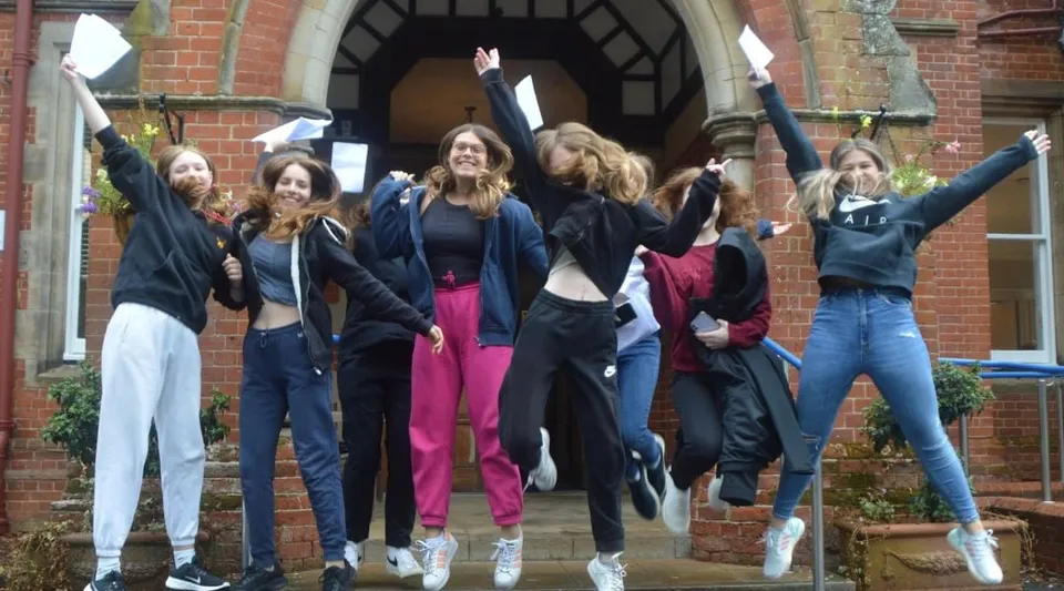 Un gruppo di studentesse del Kent College Pembury esce esultando da un edificio in mattoni.