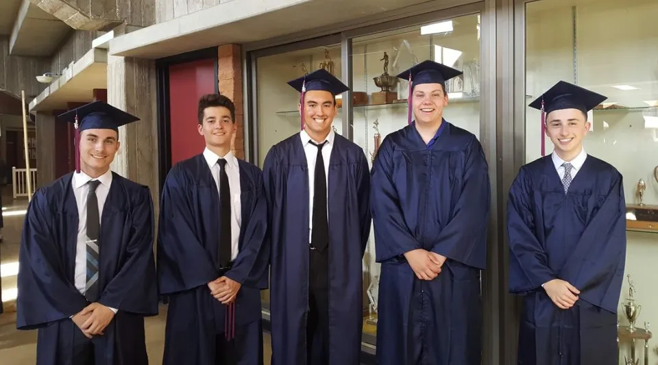 Un gruppo di cinque studenti con il tocco da diplomandi si trova davanti a una parete di vetro nel campus del Chandler Unified School District.
