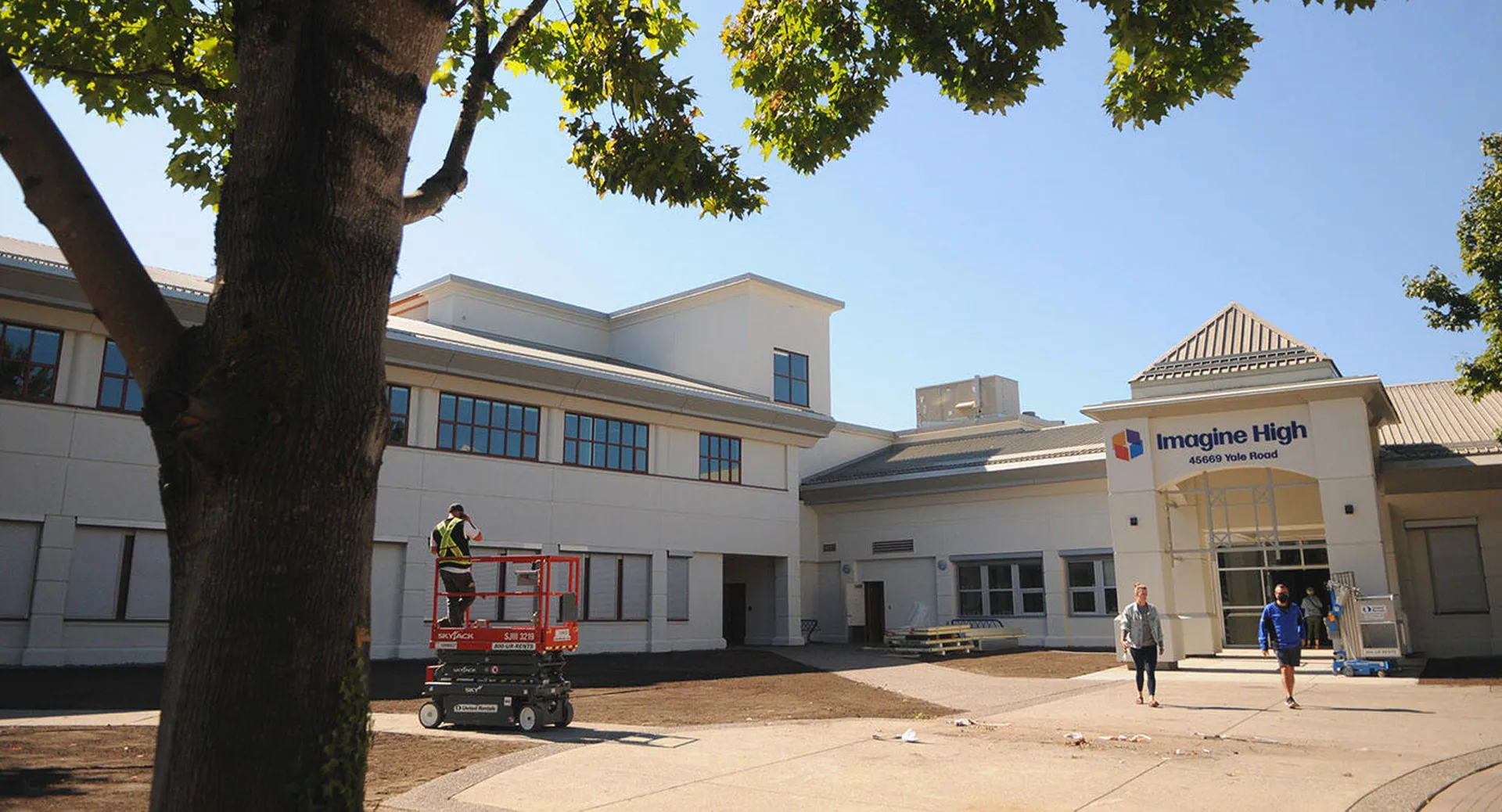 Un moderno edificio scolastico della Imagine High Integrated Arts and Technology Secondary School con un montacarichi per lavori edili in primo piano.