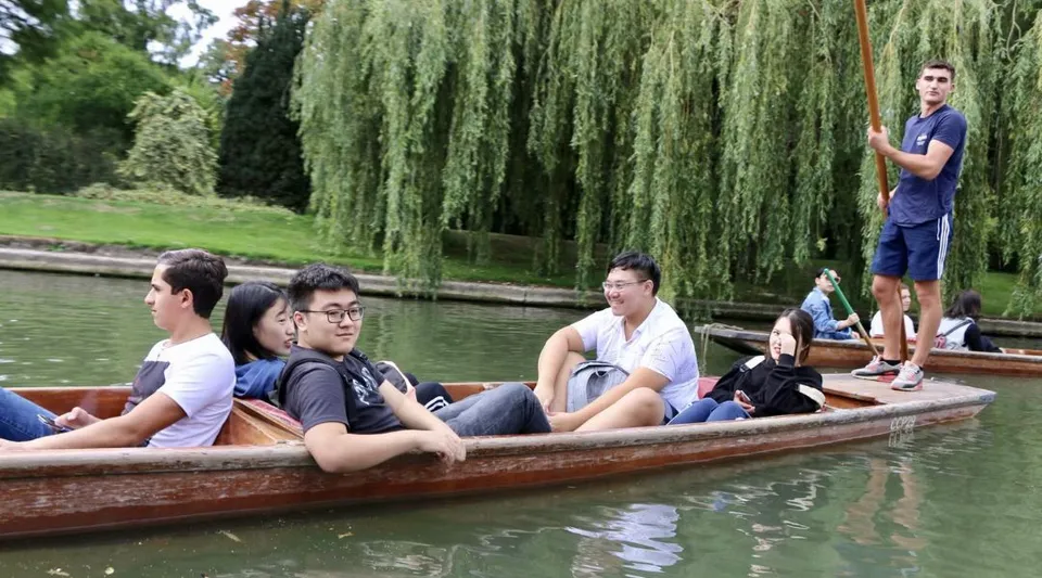 Un gruppo di studenti del St. Andrew’s College si rilassa su una barca di legno in uno stagno circondato da salici.