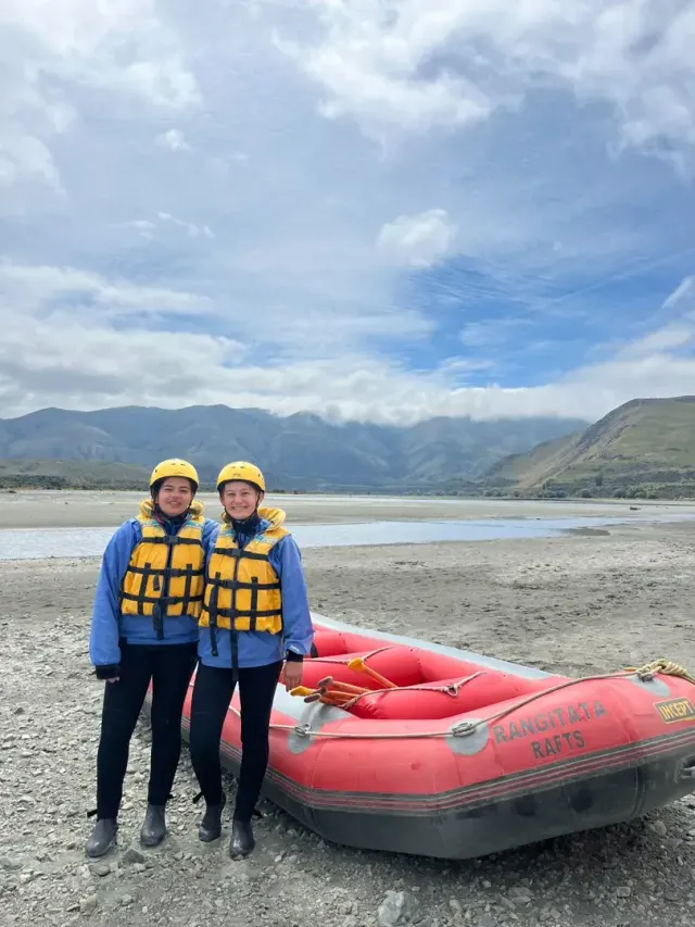 Due ragazze con casco e giubbotto di salvataggio accanto a un gommone da rafting su un fiume in Nuova Zelanda