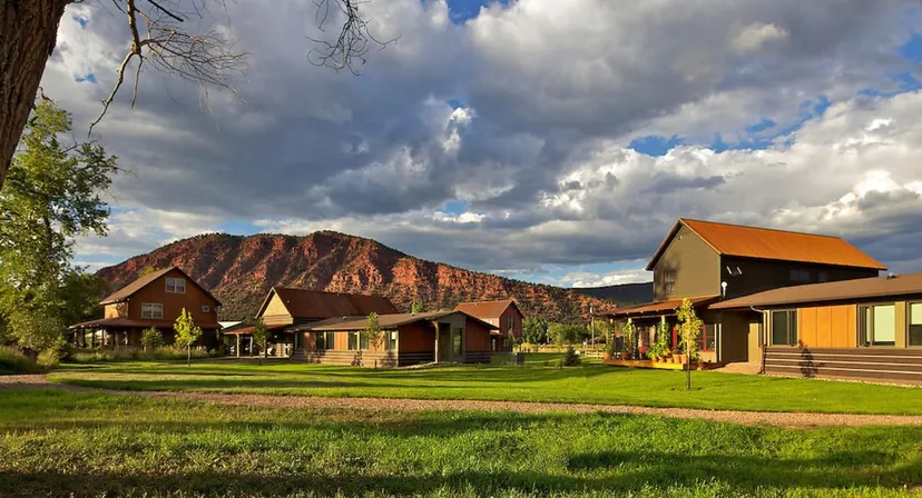 Baite rustiche in un paesaggio rurale con un campo erboso e montagne sullo sfondo nel campus della Colorado Rocky Mountain School.