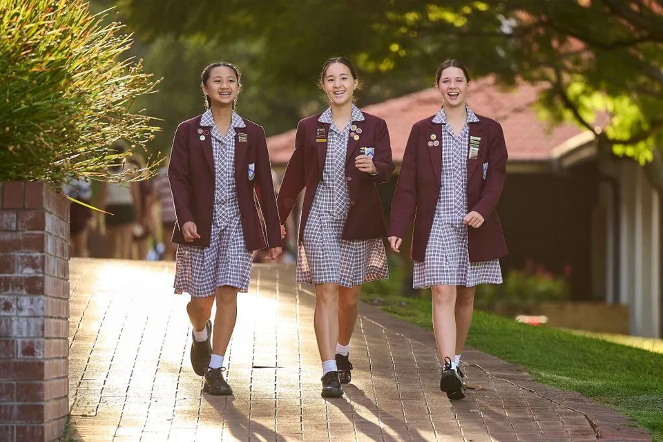 Tre studentesse della St. Mary's Anglican Girls' School camminano su un vialetto tra aree verdi ed edifici in mattoni.