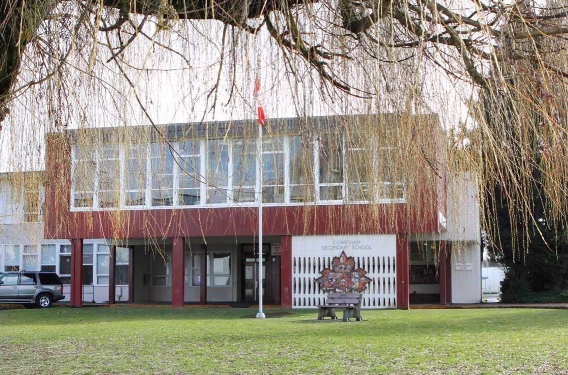 L'edificio della Cowichan Secondary School con una bandiera canadese, un prato e rami di salice in primo piano.