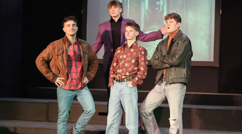 Quattro studenti della Austin Friars School sono insieme su un palco davanti a uno sfondo scuro.