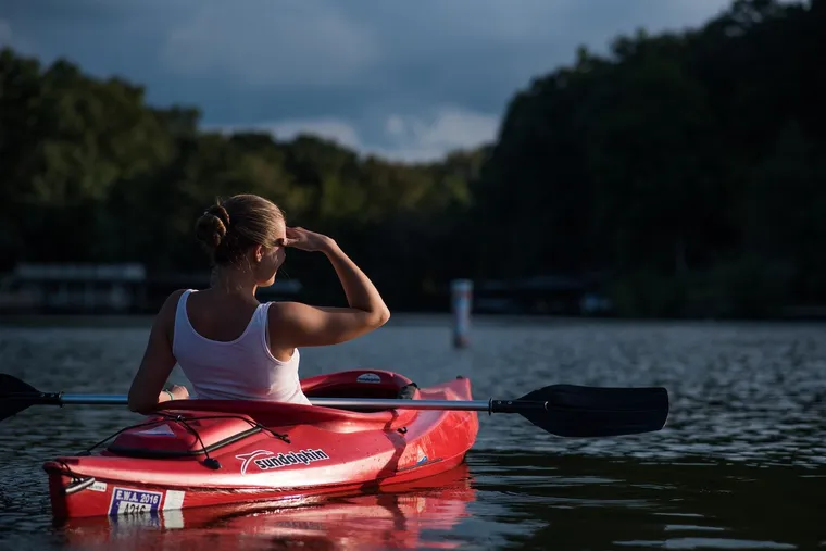 Junge Frau sitzt in einem roten Kajak auf einem See und blickt in die Ferne