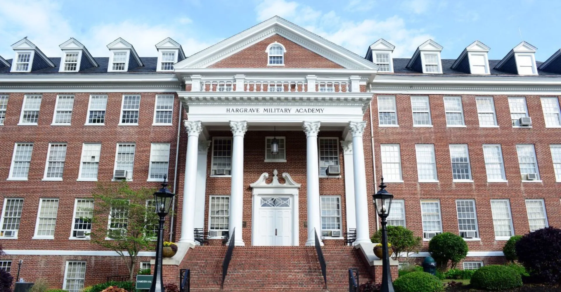 L'edificio in mattoni della Hargrave Military Academy, con una veranda a colonne e un piazzale alberato, è circondato da un vialetto lastricato.