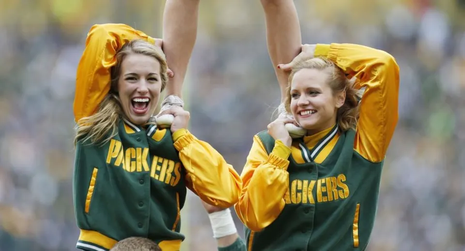 Due studentesse del Green Bay Area Public School District esultano all'aperto con maglie sportive verdi e gialle.