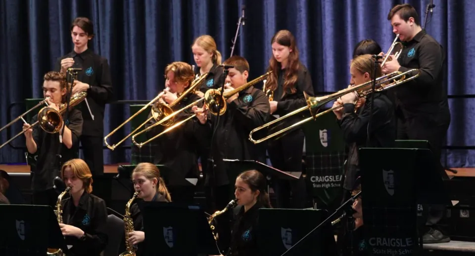 Un gruppo di studentesse e studenti della Craigslea State High School suona diversi strumenti sul palco davanti a un sipario scuro.