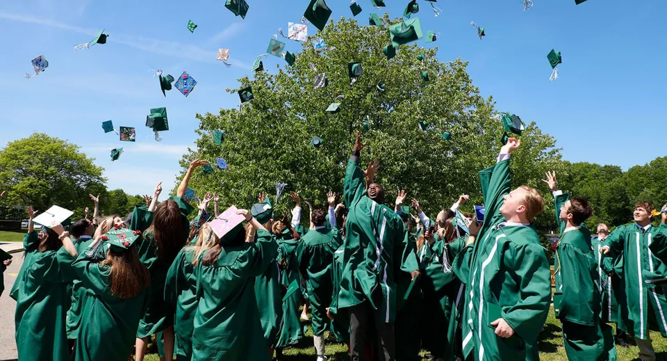 I diplomati della Rice Memorial High School sono in piedi sotto un albero e lanciano i loro tocchi in aria.