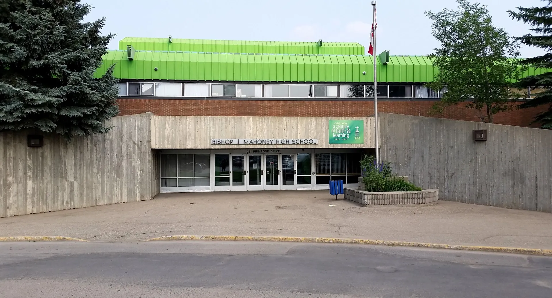 L'edificio moderno con il tetto verde si trova sull'area pavimentata della Bishop Mahoney High School, circondato da alberi e cespugli.