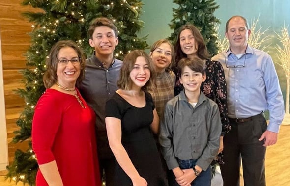 Grupo de siete personas sonriendo junto a dos árboles de Navidad iluminados