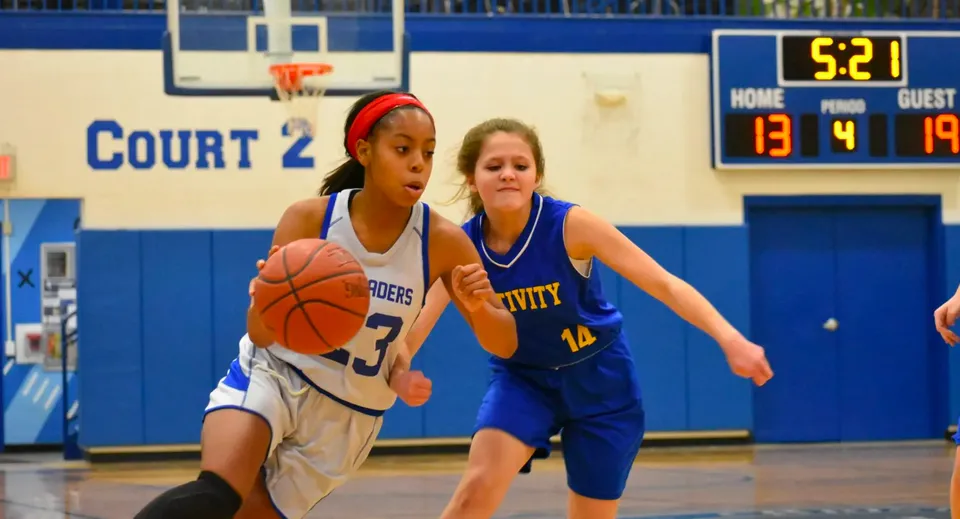Due studentesse della Christian Central Academy si contendono la palla sul campo da basket davanti a un tabellone segnapunti.