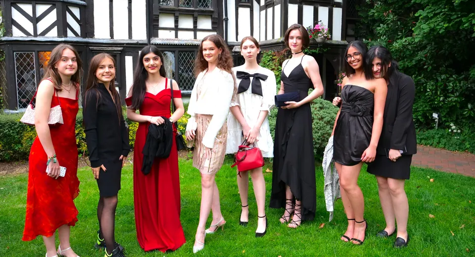 Un gruppo di donne vestite alla moda si trova davanti a un edificio storico Tudor nel campus del National Mathematics & Science College.