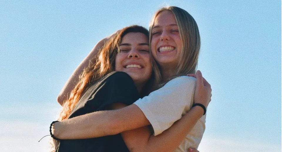 Due studentesse si abbracciano sotto un cielo limpido nel campus della Monterey Bay Academy.