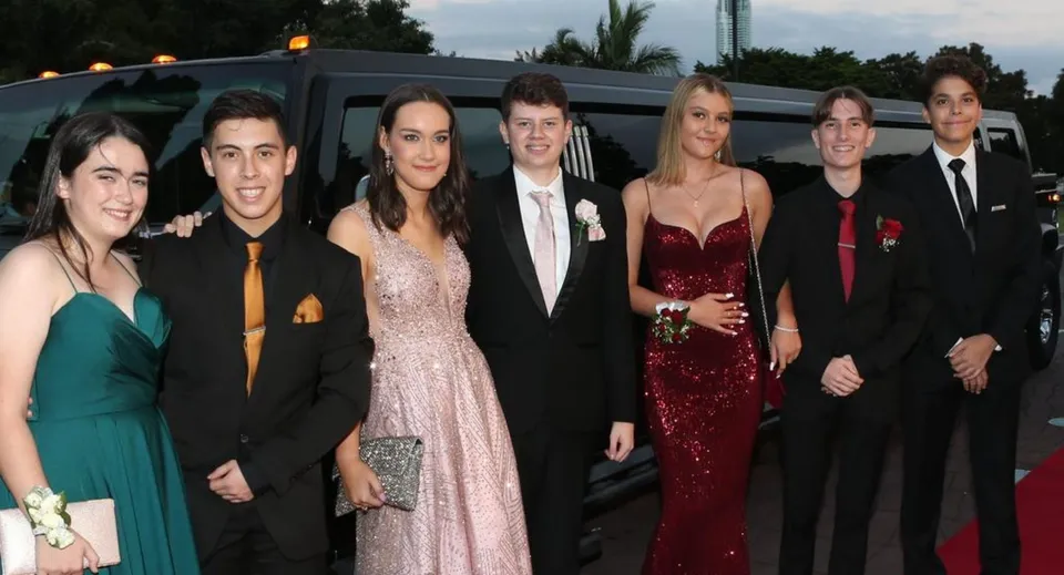 Un gruppo di studenti del Saint Stephen’s College ben vestiti posa davanti a una limousine durante un evento scolastico.