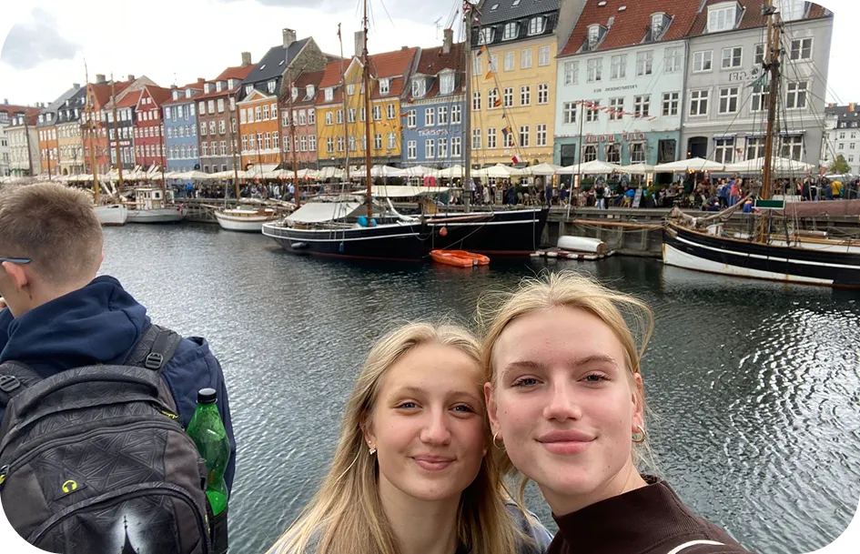 Due studentesse si fanno un selfie davanti alle case colorate e alle barche di Nyhavn a Copenhagen