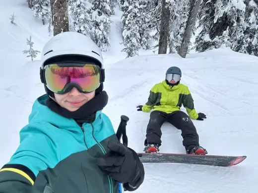 Estudiante se hace un selfie en la nieve mientras otro descansa sobre su tabla de snowboard