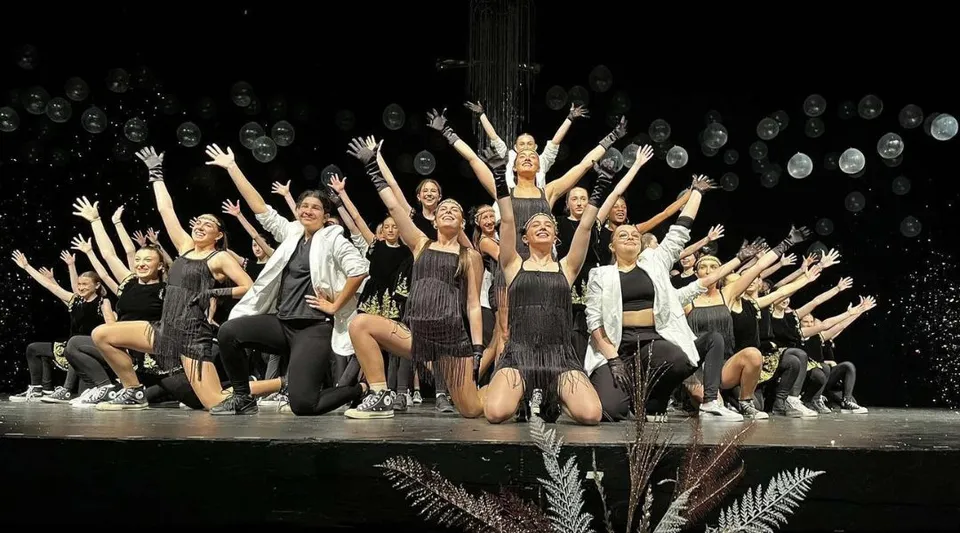 Un gruppo di ballerini della Massey-Vanier High School si esibisce in una performance su un palco con riflettori.