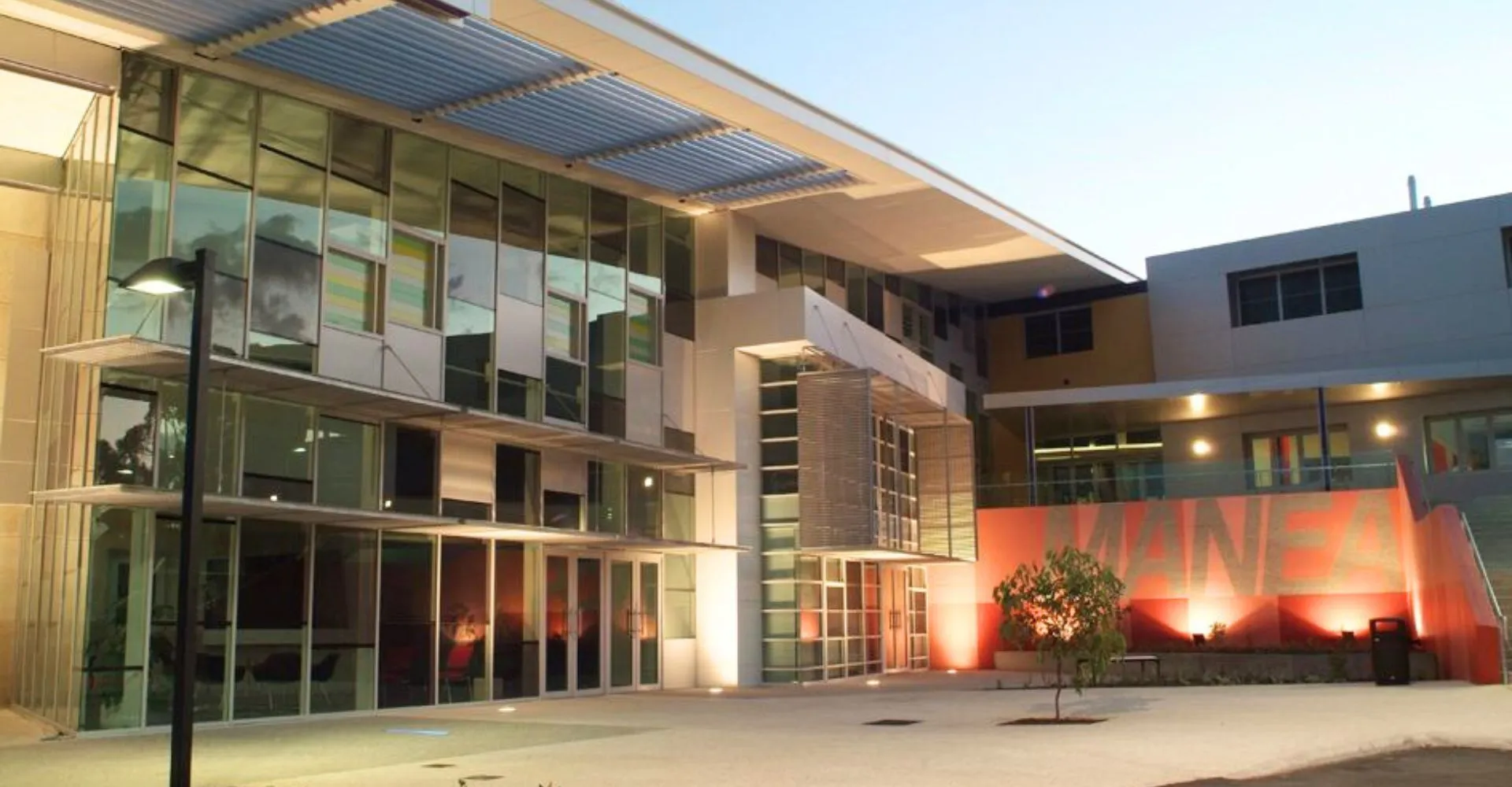 L'edificio moderno del Manea Senior College mostra una facciata in vetro con ingresso coperto e un'area esterna illuminata su un cortile pavimentato.