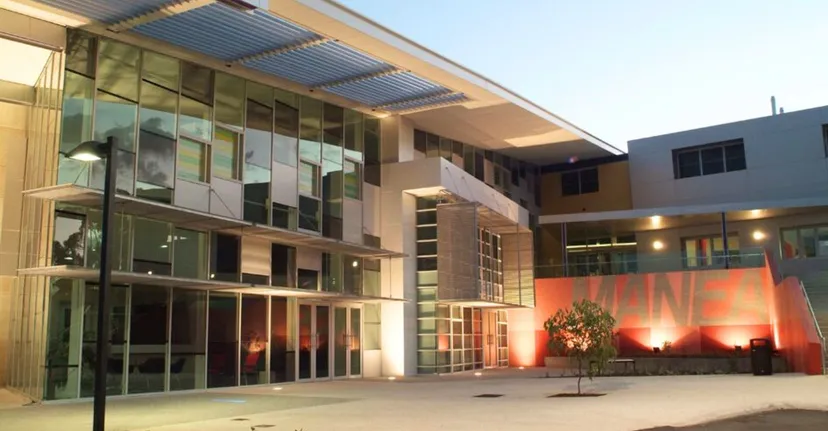 L'edificio moderno del Manea Senior College mostra una facciata in vetro con ingresso coperto e un'area esterna illuminata su un cortile pavimentato.