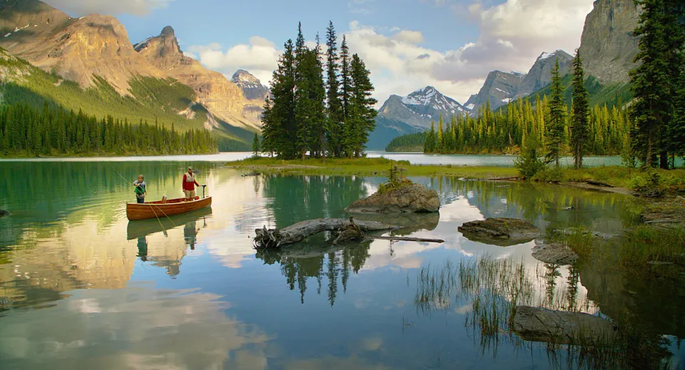 Un lago tranquillo con una piccola barca e due persone riflette le montagne sul terreno della Lord Beaverbrook High School.