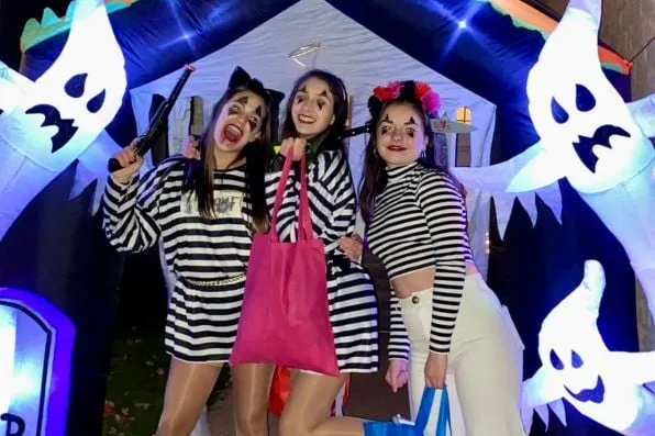 Tres chicas disfrazadas con camisetas a rayas posan entre adornos hinchables de fantasmas de Halloween