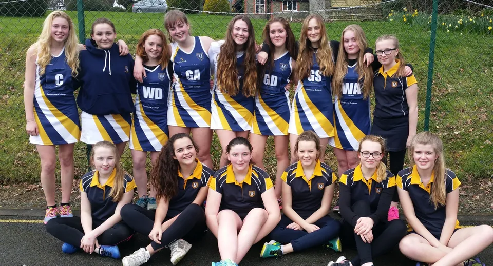 Un gruppo di giovani giocatrici di netball posa insieme sul campo sportivo del Bedstone College.
