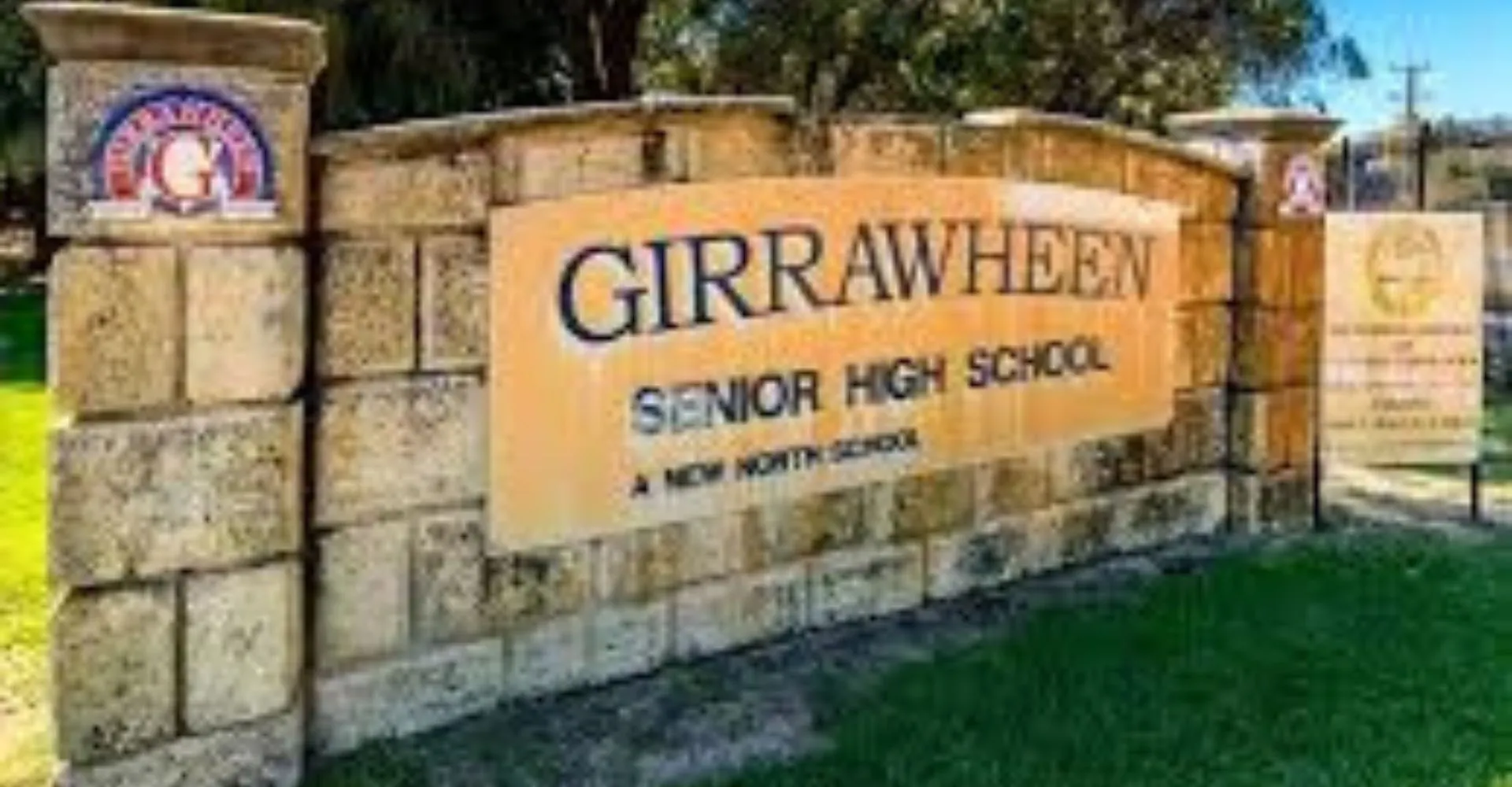 La targa in pietra con la scritta Girrawheen Senior High School si trova davanti ad alberi e edifici nel campus scolastico.