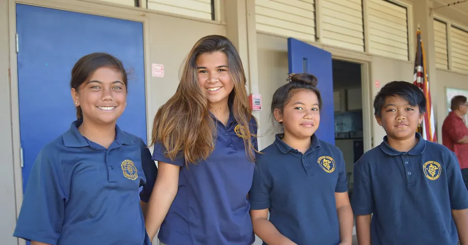 Quattro studenti della St. Anthony School sono in piedi davanti a un edificio con pareti blu e bianche.