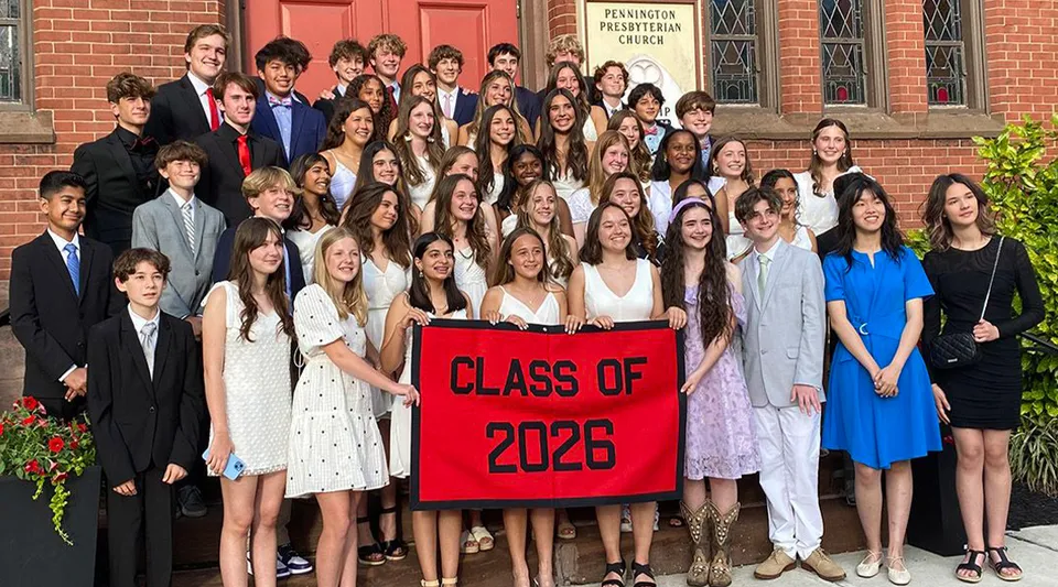 Un gruppo di studenti della The Pennington School in abbigliamento formale sta davanti a un edificio in mattoni con uno striscione della classe 2026.