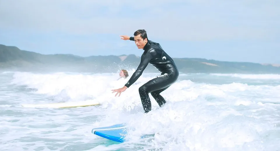 Una persona in una muta nera fa surf su un'onda nell'oceano con le montagne sullo sfondo sul terreno della Springbank School.