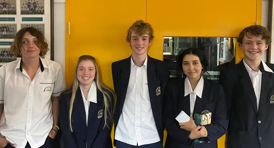 Cinque studenti posano insieme davanti a una parete gialla all'interno del campus della Bribie Island State High School.