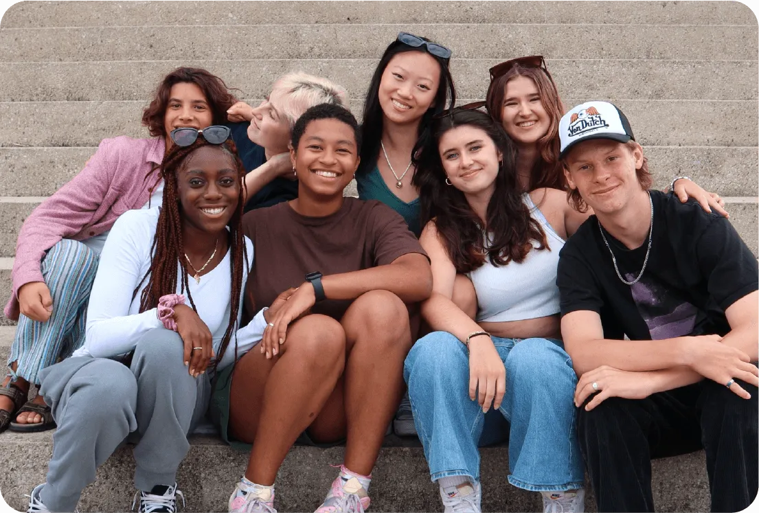 Grupo de estudiantes sentados juntos en unas escaleras sonriendo a cámara