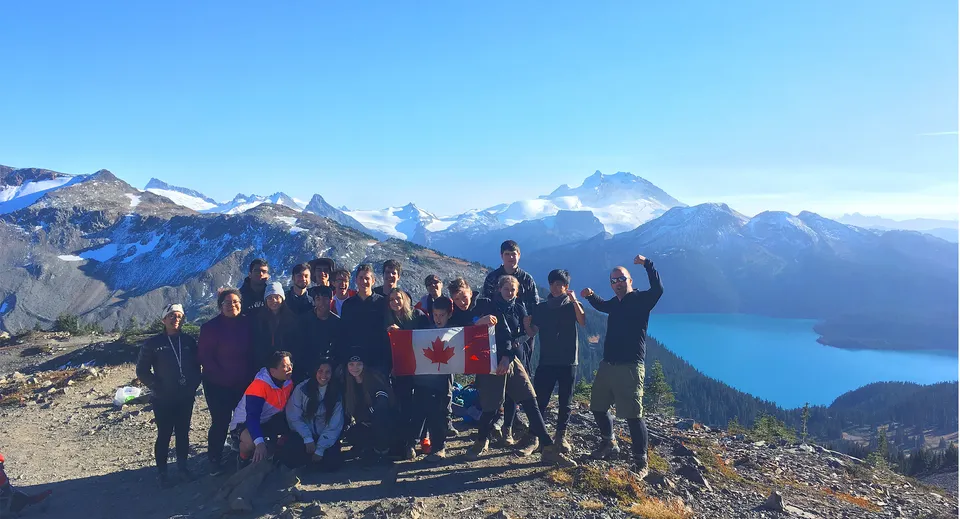 Un gruppo di studenti della Rick Hansen Secondary School si trova su un crinale montuoso con vista su cime innevate e un lago.