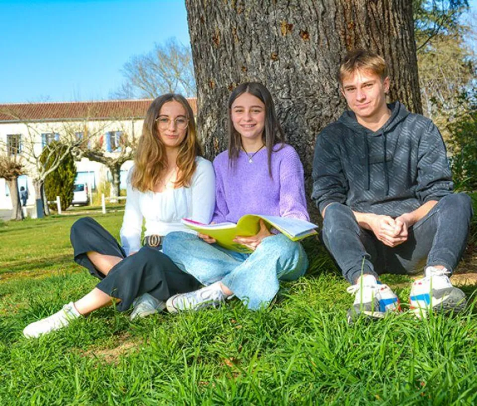 Tre studenti seduti sul prato davanti a un edificio del Campus La Salle Saint Christophe.