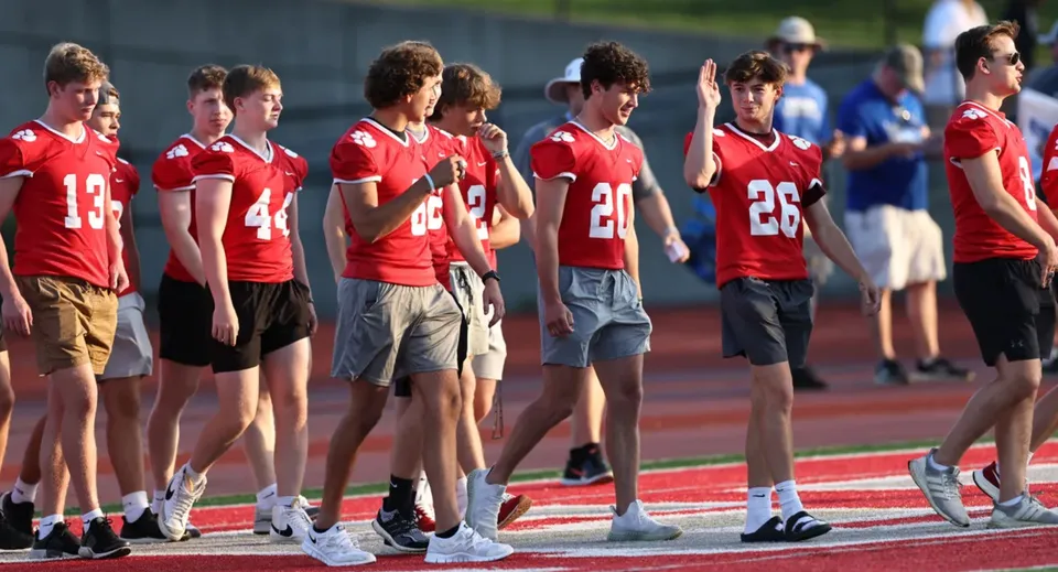 Un gruppo di studenti della Beechwood Sacred Heart School in maglia rossa si trova sul campo da calcio davanti al pubblico.
