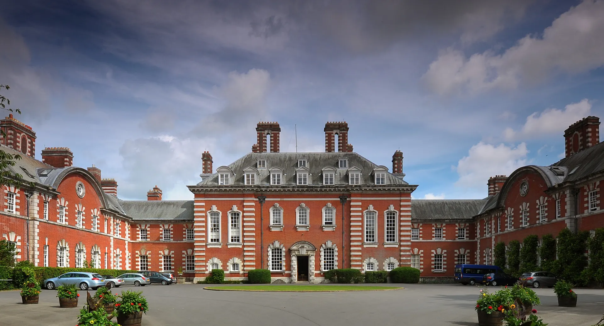 L'edificio principale della Bryanston School si trova in un cortile interno alberato con verde circostante e auto parcheggiate.