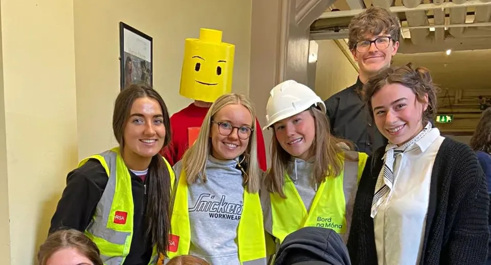Un gruppo di studenti e studentesse del St. Finian’s College con gilet ad alta visibilità e caschi posa davanti a un personaggio dei cartoni animati giallo.